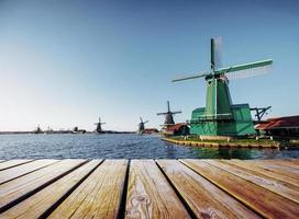 bunter frühlingstag mit traditionellem holländischem windmühlenkanal in rotterdam. Holzsteg in der Nähe des Seeufers. foto