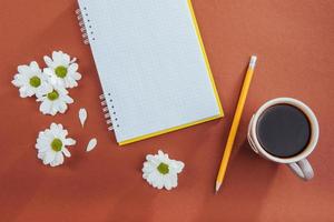 auf hölzernem Hintergrund Notebook-Bleistift, Kaffee und Blumen. foto