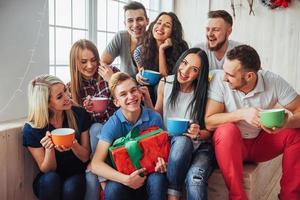 gruppe der besten freunde auf der party. lächelnde und fröhliche menschen, die auf der treppe sitzen, grüßen den geburtstag, tolles geschenk foto