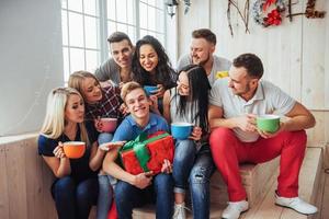 gruppe der besten freunde auf der party. lächelnde und fröhliche menschen, die auf der treppe sitzen, grüßen den geburtstag, tolles geschenk foto