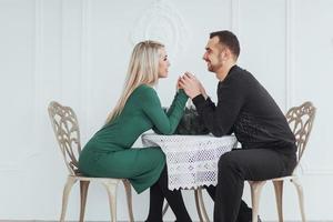 Liebe am Tisch sitzen Paar Mann und Frau mit Weingläsern auf weißem Hintergrund im Restaurant. Valentinstag Abendessen foto