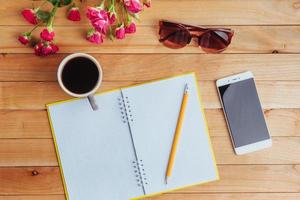 auf hölzernem Hintergrund Notebook-Bleistift, Kaffee und Blumen. foto