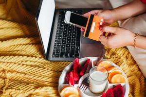 leute auf einem bett mit hand, die kreditkarte und smartphone für online-einkaufszahlung hält foto