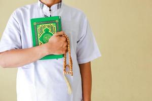 beschnittene aufnahme eines muslimischen mannes, der das heilige buch al-quran und gebetsperlen in der hand hält foto