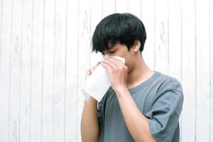 junger asiatischer mann, der zu hause in seidenpapier niest foto