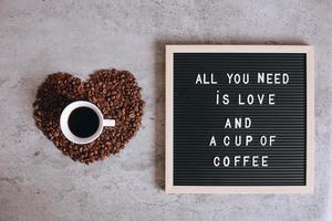 Draufsicht auf eine Tasse Kaffee auf schöner Herzform aus Kaffeebohnen mit Zitat auf dem Briefbrett sagt, alles, was Sie brauchen, ist Liebe und eine Tasse Kaffee foto