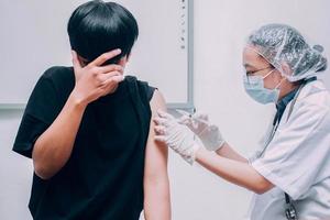 junger Patient mit Angst- oder Schreckensausdruck, der sein Gesicht bedeckt, wenn ihm vom Arzt ein Impfstoff injiziert wird foto