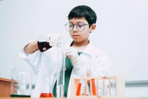 asiatischer junge student mit reagenzgläsern studiert chemie im schullabor und gießt flüssigkeit. nationaler wissenschaftstag, weltwissenschaftstag foto