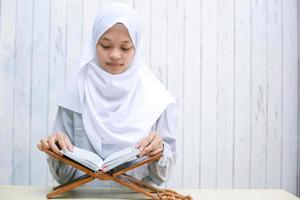 junge asiatische islamfrau mit kopftuch, die das heilige buch von al-quran liest foto