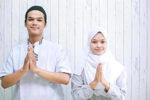 asiatisches muslimisches paar, das einen muslimischen händedruck in die kamera macht, um gäste willkommen zu heißen oder auf der eid mubarak-feier zu begrüßen foto