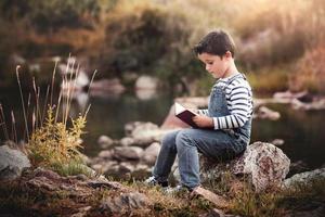 Kind sitzt und liest ein Buch auf dem Feld foto