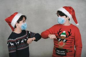 Frohe Weihnachten, zwei Kinder mit medizinischer Maske und Weihnachtsmann-Hut, Ellbogen, soziales Distanzierungskonzept foto