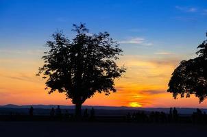 Silhouetten von Bäumen und Menschen, die einen erstaunlich bunten roten Sonnenuntergang beobachten foto