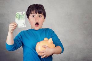 überraschtes Kind, das Geld in einem Sparschwein spart foto