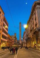 bologna, italien viele menschen gehen die straße hinunter zu zwei mittelalterlichen türmen foto