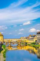 brücke ponte vecchio mit bunten gebäuden beherbergt über dem fluss arno blau reflektierendes wasser foto