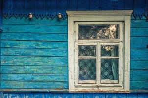 schäbige Holzwand und Fenster mit Tüll aus blauem altem Haus im Dorf foto