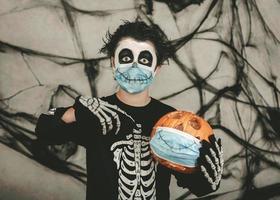 fröhliches halloween, kind mit medizinischer maske in einem skelettkostüm mit halloween-kürbis foto