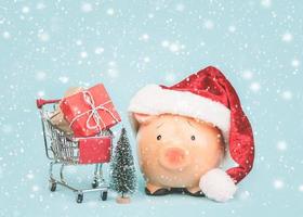 weihnachtskonzept hintergrund. sparschwein mit weihnachtsmütze und einkaufswagen mit weihnachtsgeschenken foto