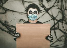 Fröhliches Halloween. Kind mit medizinischer Maske in einem Skelettkostüm mit braunem Brett foto