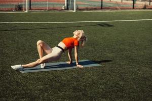 Schöne Blondine beim Stretching auf dem Rasen eines Fußballfeldes foto