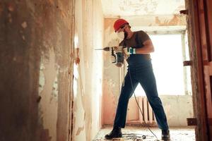 Baumeister mit Perforator bohrt Löcher in Betonwand foto