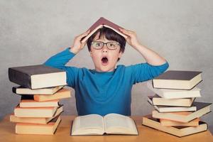 überraschter Junge mit Büchern auf einem Tisch foto