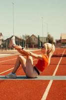 Junge Blondine schüttelt Bauchmuskeln auf einer Sportmatte auf der Straße foto