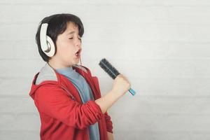 lustiges kind in den kopfhörern, die mit haarbürste singen foto