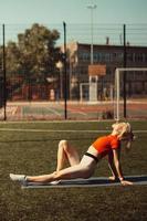 Schöne Blondine beim Stretching auf dem Rasen eines Fußballfeldes foto