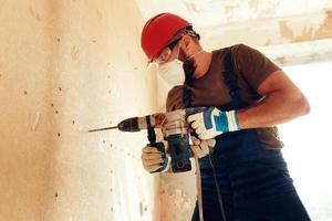 Baumeister mit Perforator bohrt Löcher in Betonwand foto