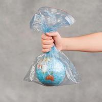 Kinderhand, die Erdkugel in transparenter Plastiktüte hält foto