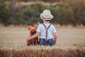 Junge umarmt Teddybär im Weizenfeld foto