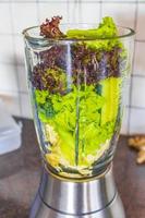 Grüner gesunder Smoothie mit Gemüse-Obstsalat-Grüns im Mixer. foto