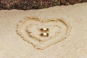 Trauringe in einem Herzen aus Sand. Flitterwochen in Thailand. foto