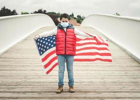 kind mit medizinischer maske schwenkt die flagge der vereinigten staaten foto