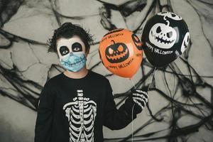 Fröhliches Halloween. kind mit medizinischer maske in einem skelettkostüm mit halloween-ballons foto