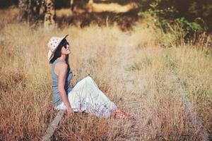 glückliche und lächelnde junge Frau, die auf dem Feld sitzt foto