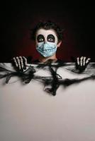Fröhliches Halloween. kind, das eine medizinische maske in einem skelettkostüm trägt, das ein leeres brett hält foto