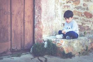 Trauriges Kind, das neben einer Tür sitzt foto