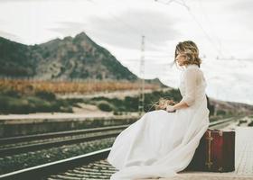 nachdenkliche Braut mit rotem Koffer auf den Bahngleisen foto