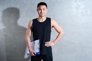 junger asiatischer persönlicher trainer, der auf grauem hintergrund aufwirft foto