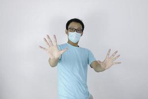 junger asiatischer mann, der eine hygienemaske trägt, hat angst oder panik mit gestikulierender stopphand. Angst vor einer Coronavirus-Infektion oder Atemwegserkrankungen wie Grippe. indonesischer Mann isoliert auf weißem Hintergrund foto