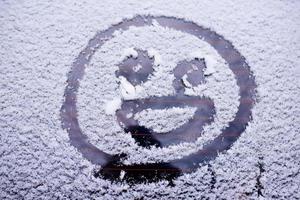 fröhliches Smiley-Gesicht auf der verschneiten Windschutzscheibe eines Autos foto