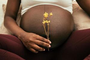 schwangere Frau, die eine Blume vor seinem Bauch hält foto