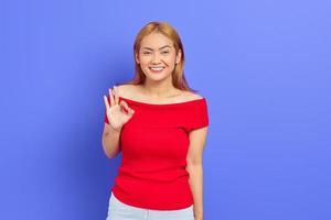 Porträt einer lächelnden positiven asiatischen Frau, die posiert und eine okay-Geste macht, isoliert auf violettem Hintergrund foto