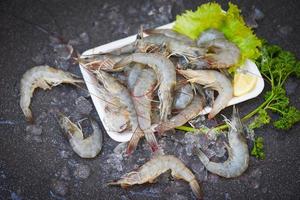 frische Garnelengarnelen zum Kochen mit Gewürzzitrone auf dunklem Hintergrund im Fischrestaurant, rohe Garnelen auf Tellerplastikschale, Draufsicht foto