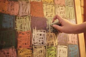 Nahaufnahme der Handkreativität des kleinen Mädchens, die die Kunstfarbe an der Tafel in der Freizeiterziehung der Kinder durch bunte Kreide-, Rosa-, Gelb-, Grün-, Blau- und Glücksdesignillustrationen zeichnet. foto