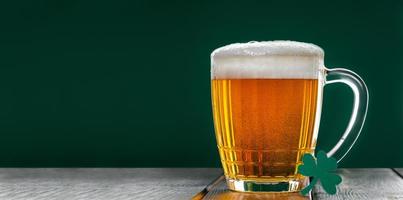 Becher helles Bier mit Schaum auf grünem Hintergrund. traditionelles irisches Getränk.