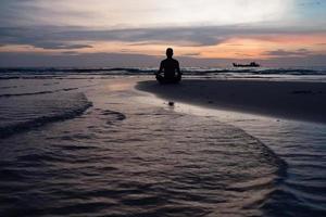 Silhouette des Mannes meditieren am Strand bei Sonnenuntergang foto